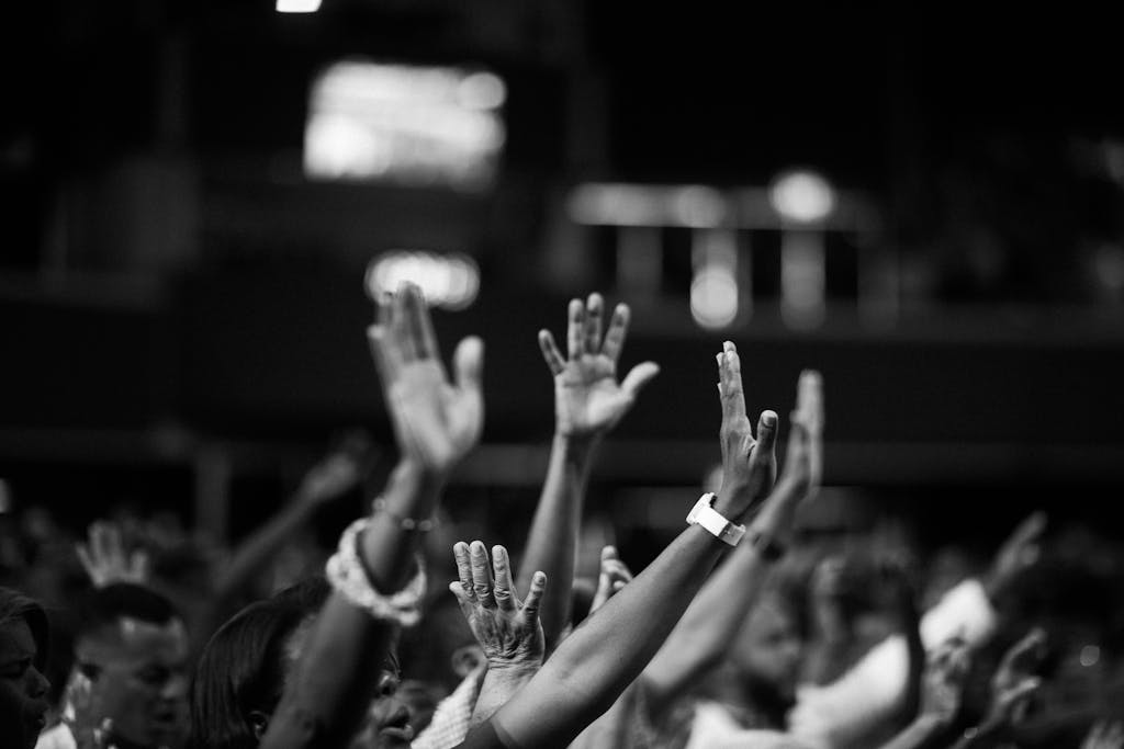 A group of people raising hands in a black and white, singing songs of praise