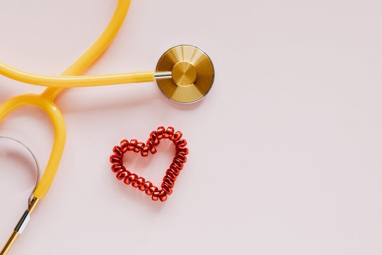 A yellow stethoscope near small red bead heart.