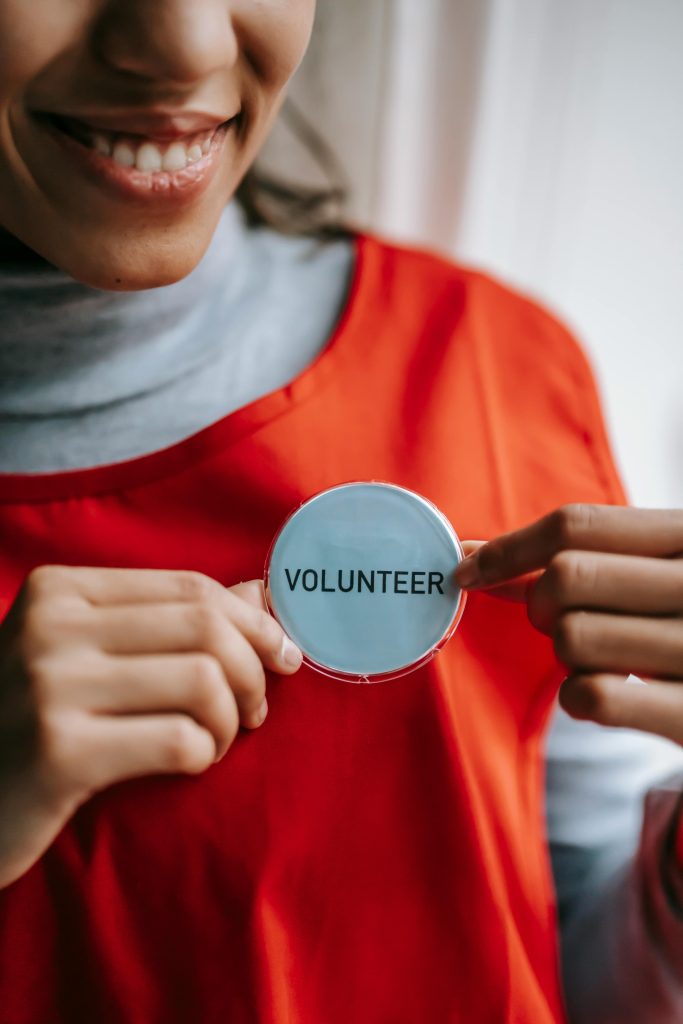 A woman in an orange shirt holding up a volunteer button on her shirt