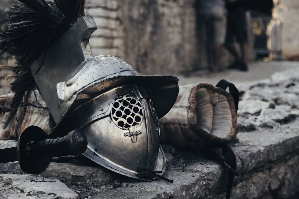 An armor helmet, sword, and glove against a stone wall depicting historical combat gear.