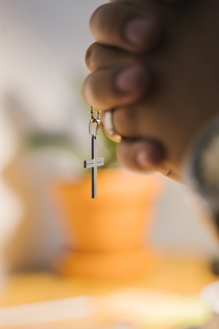 Close-up of hands clasped in prayer holding a cross pendant.